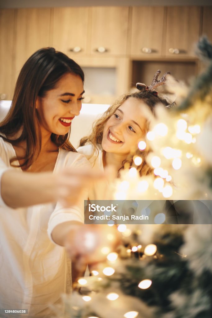 Lovely girls enjoying while decorating Christmas tree. Older and younger sister are happy to decorate Christmas tree and spend New Year's Eve together. They are smiling and enjoying great time during Winter vacation. Family Stock Photo