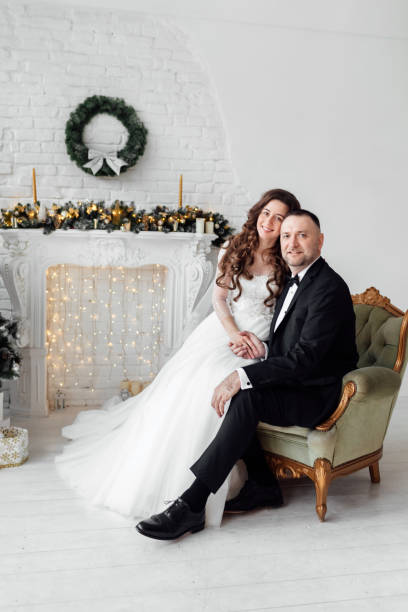 jovem casal apaixonado de noiva e noivo posando em estúdio ao fundo decorado com árvore de natal no dia do casamento no natal. aproveite um momento de felicidade e amor. - christmas wedding bride winter - fotografias e filmes do acervo