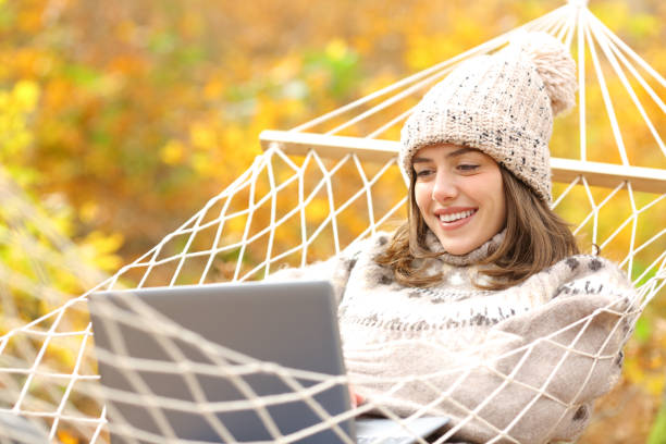 Photo of Happy woman on hammock using laptop in autumn