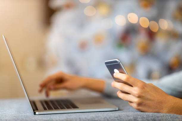 istock Cropped Hands Of Man Using Smart Phone and Laptop Against Christmas Tree 1284810696