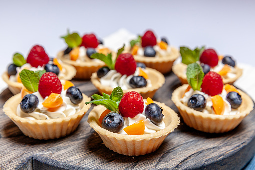 Fruit and berry tartlets dessert assorted on wooden tray. Closeup of delicious pastry sweets pies colorful cakes with fresh natural raspberry blueberry and cheese cream. French bakery catering