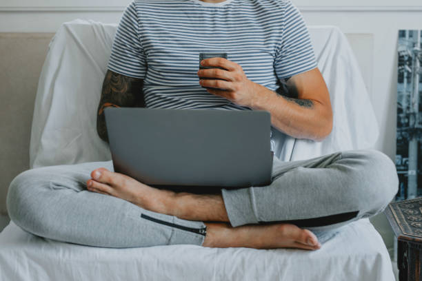 trabalhando em casa: jovem empresário anônimo participando de uma conferência online enquanto senta e bebe café em sua sala de estar - tattoo shirt caucasian one person - fotografias e filmes do acervo