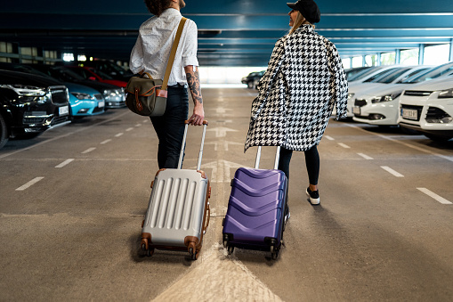 Young couple arriving at the airport and walking with luggage in garage, back view