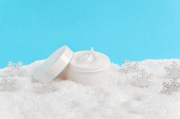 istock Opened face cream jar in snow and snowflakes on blue background. Moisturizing hand creme, face mask or body lotion. Winter skin care cosmetic products. Seasonal skin protection from cold weather 1284817382