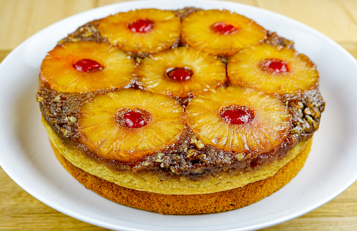 A freshly made upside down cake on a white plate set on a wooden background