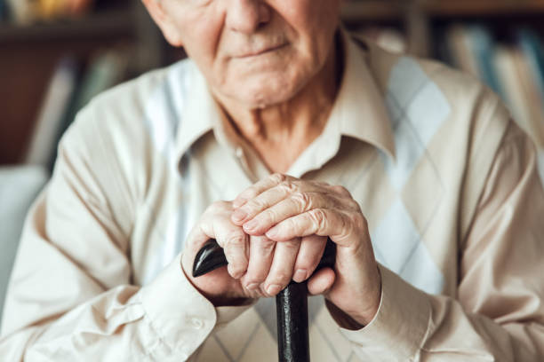 istock Senior man alone sitting at library with walking stick close-up 1284822298