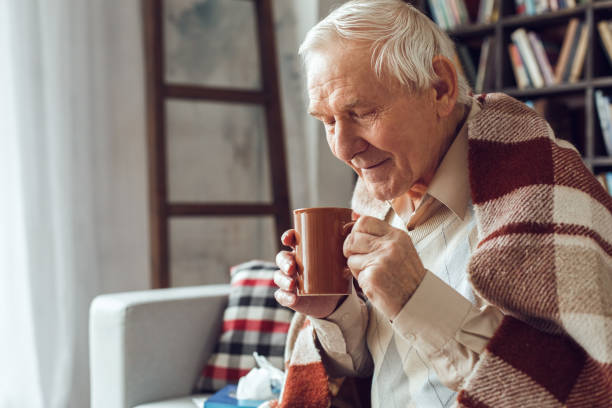 istock Senior man alone sitting at library sick covered with plaid drinking tea joyful 1284822301