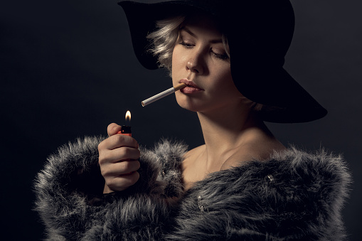 Young woman luxury style isolated wearing fur coat and hat lighting a cigarette smoker