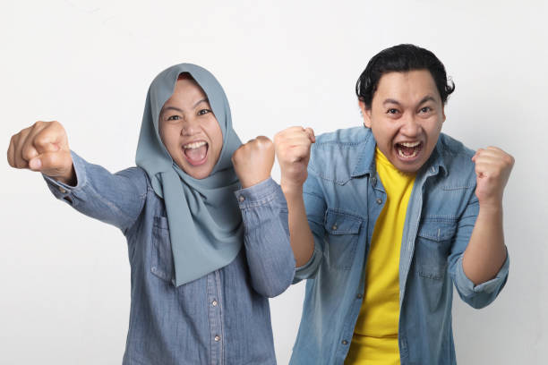 Yes we win. Portrait of positive cheerful married Asian muslim couple hear winning news raise fists and  shout Yes we win. Portrait of positive successful cheerful married Asian muslim couple hear winning news raise fists and  shout malay couple stock pictures, royalty-free photos & images