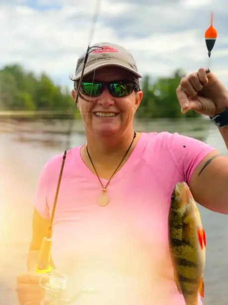 Woman fisherman, wearing a pink shirt, spending the day on her pontoon. Series of photographs shows the woman, fishing, pontoon riding on The Menominee River in Wisconsin and upper Michigan, and enjoying the outdoors.