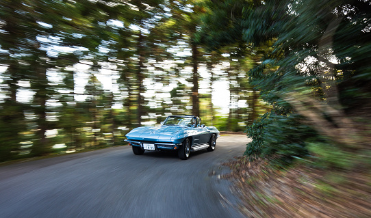 Gozaisho mountain forest drive October/25/2020 a classic 1964 Corvette Stingray is driving along a narrow mountain forest road with blurred movement to show to speed of the vehicle. The Chevrolet Corvette is a classic American Muscle car that is still in production today. This one was imported to Japan which is quite rare especially for an old classic in such pristine condition.