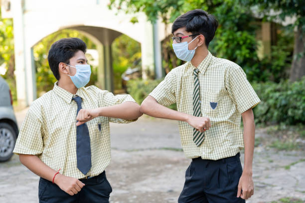 Students in the school practicing alternative greeting for safety and protection during COVID-19. Two kid in medical mask outside classroom greeting each other with elbow bumps while maintaining social distance at school campus - Concept of school reopen,back to school with safety measures and new normal lifestyle. teenagers only teenager multi ethnic group student stock pictures, royalty-free photos & images
