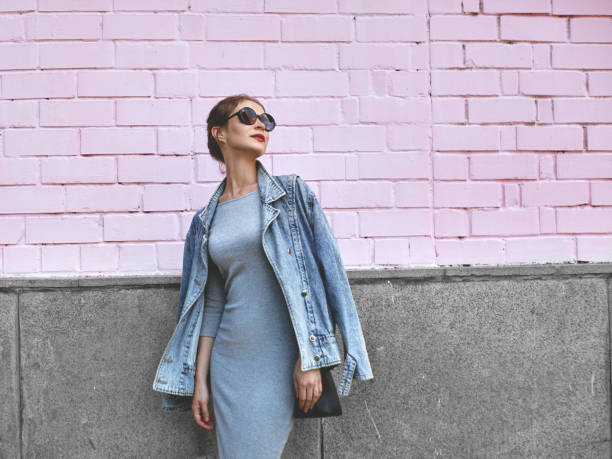 estilo de calle shoot mujer en la pared rosa. swag chica con chaqueta de jeans, vestido gris, gafas de sol. estilo de vida de moda al aire libre - bien vestido fotografías e imágenes de stock