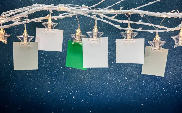 empty photo frames or notes hanging on bare twig with glowing star clothespins. christmas decoration