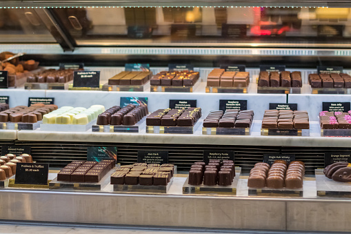 A close up of a shop window of a chocolate factory in Garmisch in Southern Germany. They create and produce varied versions of some beautifully presented chocolates and sweet treats. In the window is multiple variations of toppings and flavours.