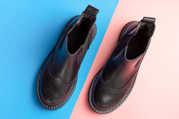 Black leather autumn boots on blue and pink background, top view