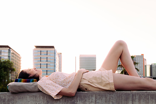 young woman lying on her backpack at sunset in front of the city, concept of youth and traveler lifestyle, copy space for text