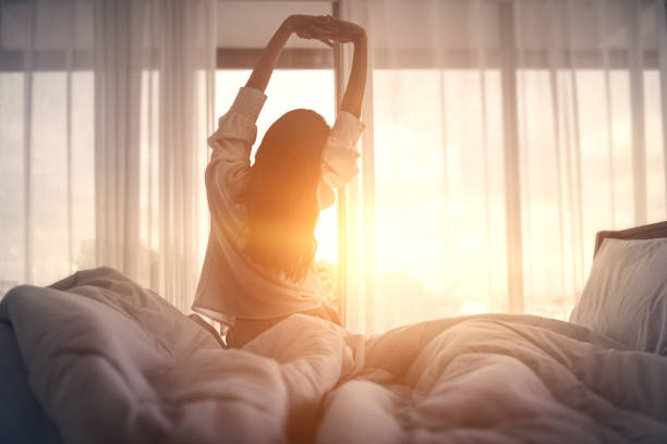 mujer feliz estirando en la cama después de despertarse. feliz jovencita saluda buenos días. - despertar fotografías e imágenes de stock