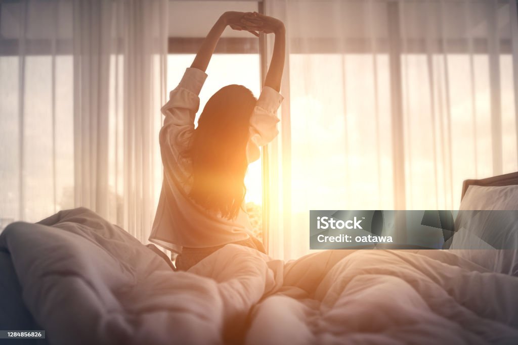 快樂的女人醒來後在床上伸展。快樂的年輕女孩迎接美好的一天。 - 免版稅睡覺圖庫照片