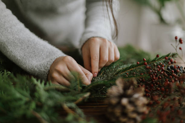 istock Female hands holding branches and making rustic christmas wreath on table with pine cones, berries 1284856866