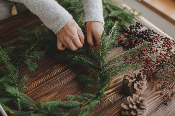 istock Hands holding pine cone and green fir branches on wooden table, making rustic christmas wreath 1284857586