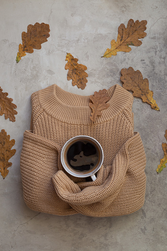 Autumn composition. Cup of coffee, sweater and autumn leaves on stone background. Flat lay with copy space