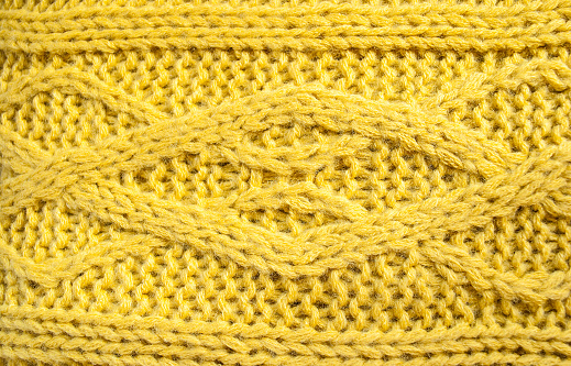 Texture of yellow knitted sweaters ornament. Chain Cable stitch knit fabric background close up, selective focus