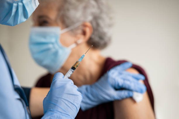 arzt macht impfung an seniorin mit chirurgischer maske - arzthelferin fotos stock-fotos und bilder