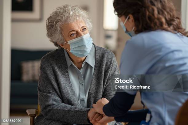 Female Doctor Consoling Senior Woman Wearing Face Mask During Home Visit Stock Photo - Download Image Now
