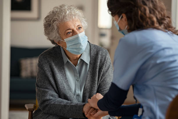 kobieta lekarz pocieszający starszą kobietę noszącą maskę na twarz podczas wizyty domowej - patient women adult home interior zdjęcia i obrazy z banku zdjęć