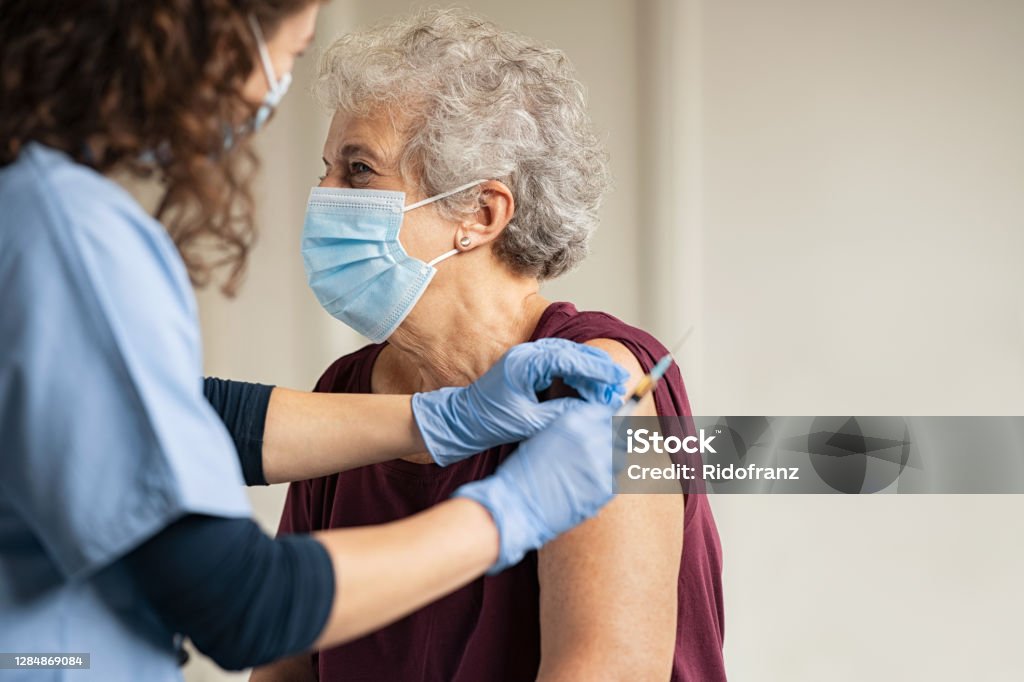 Doctor giving Covid vaccine to senior woman General practitioner vaccinating old patient in private clinic with copy space. Doctor giving injection to senior woman at hospital. Nurse holding syringe and using cotton before make Covid-19 or coronavirus vaccine. Vaccination Stock Photo
