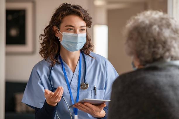 młody lekarz odwiedza starszą kobietę z maską chirurgiczną - female doctor doctor medical instrument nurse zdjęcia i obrazy z banku zdjęć