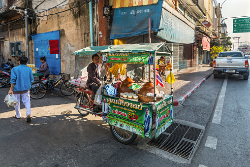 Bangkok, Thailand - December 7, 2019: Local hawker on his bicycle selling hot food on the streets of Bangkok, Thailand.