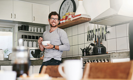 Shot of a young man standing in the kitchen and having a bowl of food at home