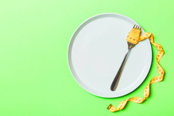 istock Strict diet concept with empty space fro your design. Top view of plate with fork in measuring tape on green background 1284879127