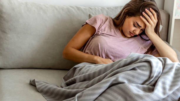 Women suffering from stomachache. Photo of young woman in painful expression holding hands against belly suffering menstrual period pain, lying sad on sofa, having tummy cramp in female health concept. Women suffering from stomachache irritable bowel syndrome photos stock pictures, royalty-free photos & images