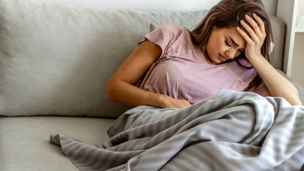 Women suffering from stomachache. Photo of young woman in painful expression holding hands against belly suffering menstrual period pain, lying sad on sofa, having tummy cramp in female health concept. Women suffering from stomachache photos of anorexia pictures stock pictures, royalty-free photos & images