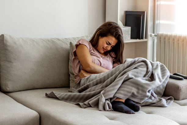 Unhappy woman holding hands on stomach suffering from abdominal pain. Unhappy woman holding hands on stomach suffering from abdominal pain with eyes closed. Women having menstrual period, food poisoning, gastritis or diarrhea. Girl feeling unwell sitting in living room. endometriosis stock pictures, royalty-free photos & images