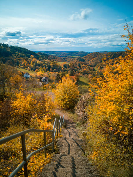 istock Ancient stone staircase on castle ruins with metal railing leading down to mountain view of valley surrounded by hills covered with colorful fall forest on sunny autumn day.Rural landscape,cloudy sky 1284880815