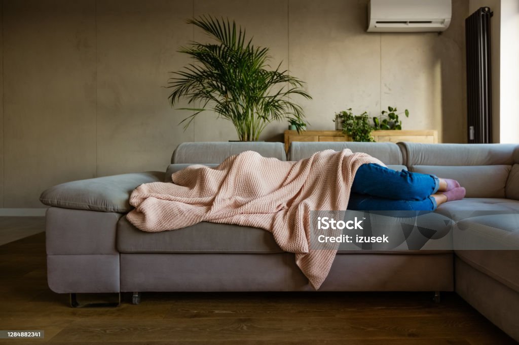 Young woman sleeping under blanket Young woman lying down on sofa in living room covered by blanket. Unrecognizable person. Sofa Stock Photo