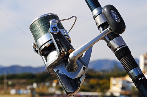 Daiwa fishing reel and rod with the beach to the rear at Puerto Cabopino, Marbella, Spain.