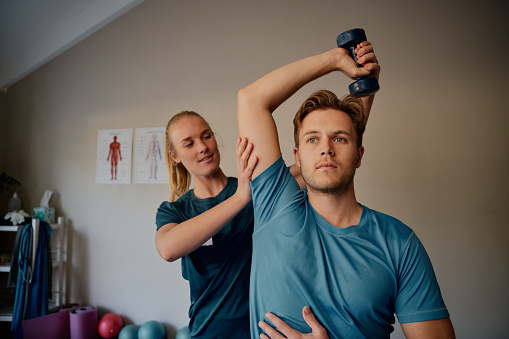 Young physiotherapist helping man exercise with dumbbells