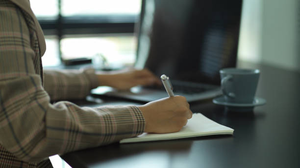 istock Female hand writing on notebook while working with laptop in office room 1284883717