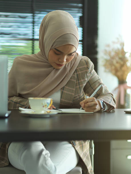 istock Asian muslim writing on notebook on office desk with cup and laptop 1284883736