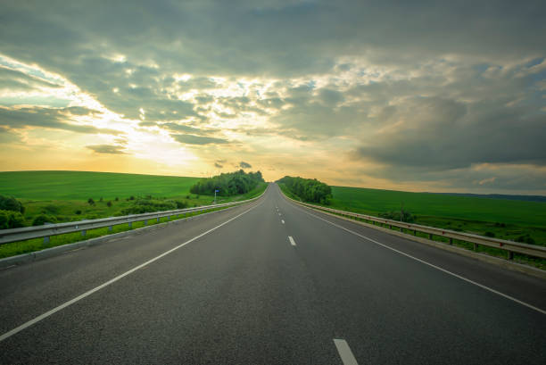 istock Landscape with empty asphalt road at sunset. Cloudy sky and green meadows 1284885885