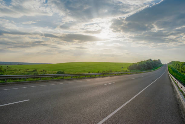 istock Empty asphalt road at sunset. Cloudy sky and green meadows 1284885901