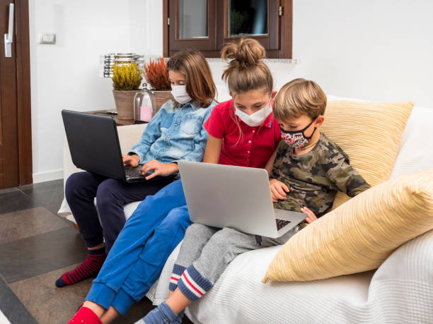 istock Children with masks coronavirus study in lockdown with laptop on the sofa at home, using the wi-fi network.