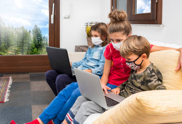 istock Children with masks coronavirus study in lockdown with laptop on the sofa at home, using the wi-fi network.