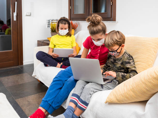 Children with masks coronavirus study in lockdown with laptop on the sofa at home, using the wi-fi network.
