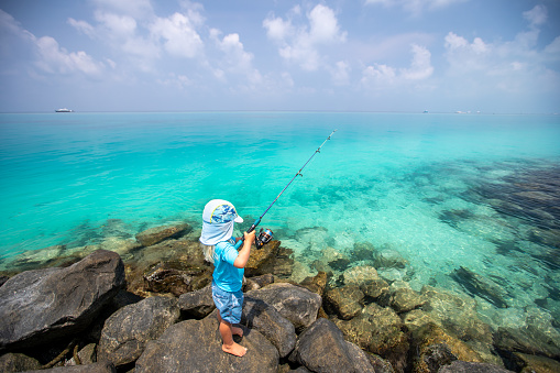 A young boy fishes in crystal clear emerald waters.